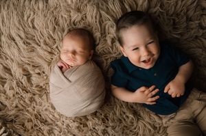 Two sleeping babies laying together on tan shag carpet, one swaddled in white and one in a navy shirt.
