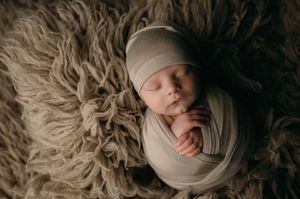 Peaceful sleeping newborn baby wrapped in beige swaddle lying on fluffy brown fur blanket.