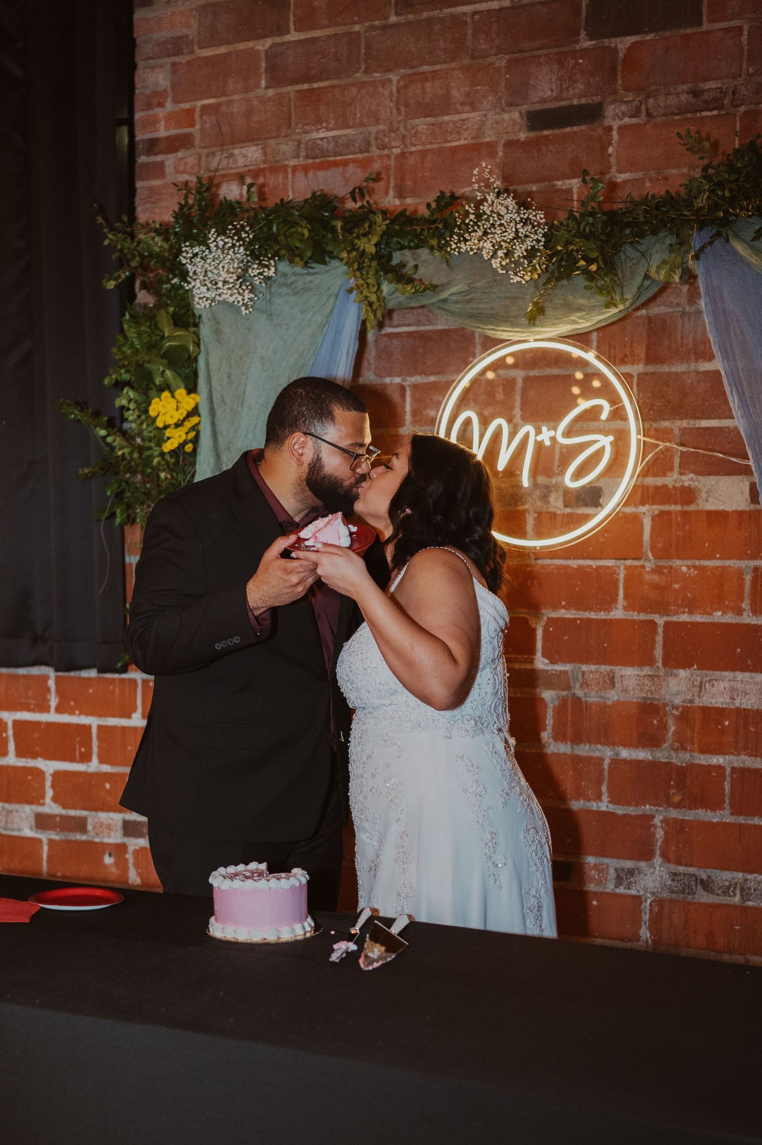A romantic moment shared between a couple in white attire against a rustic brick wall backdrop at a wedding reception.