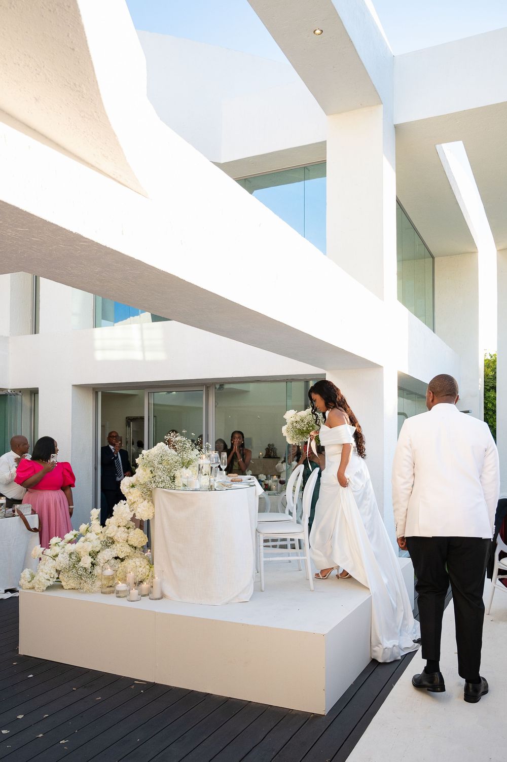 Elegant wedding reception setup in a modern white venue with architectural beams and floral arrangements.