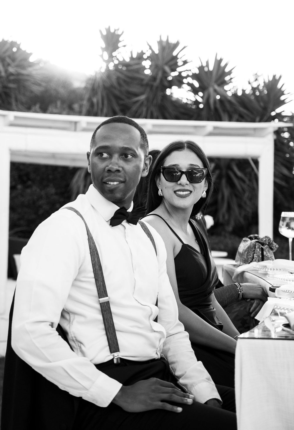 Black and white portrait series shows a couple enjoying a sunny outdoor gathering in formal attire.