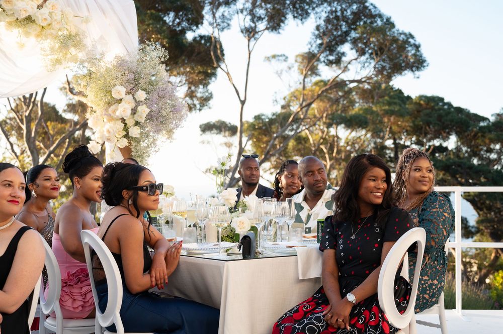 People enjoying an outdoor dining event with table settings under trees during golden hour.