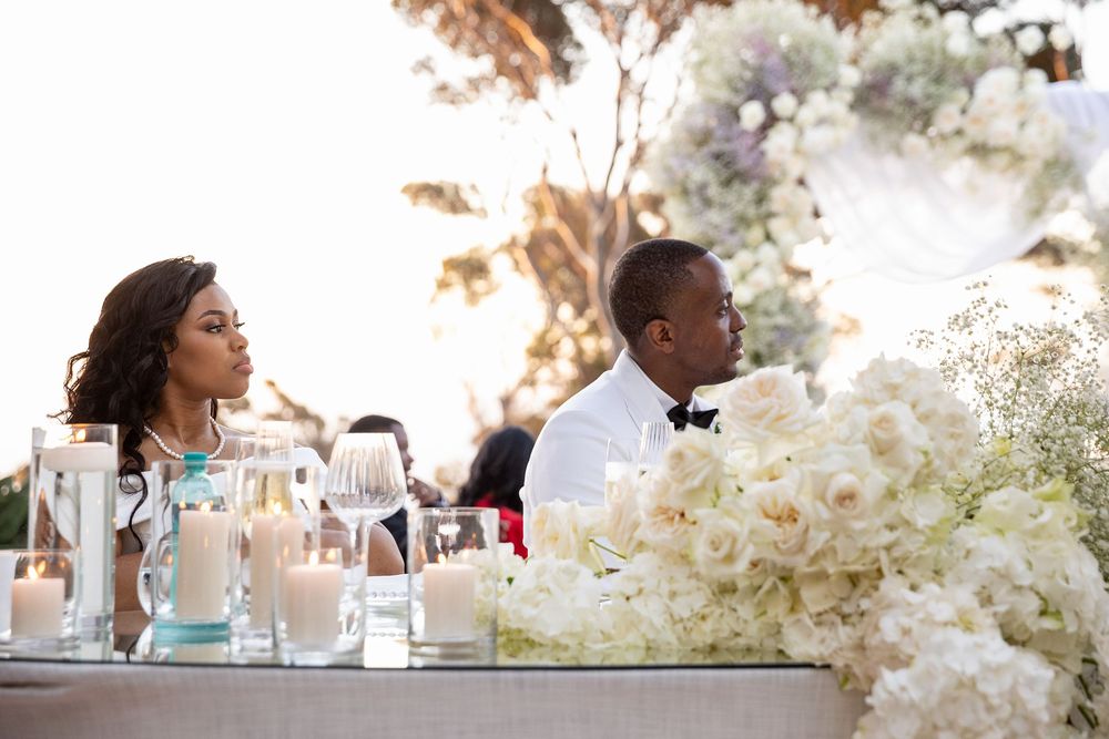 Elegant wedding reception table setting with white floral centerpieces and glassware in outdoor garden setting.