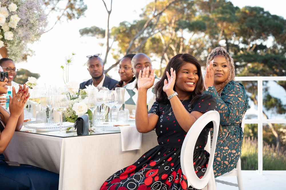 Groups of wedding guests sharing laughter and conversation around elegant reception tables with centerpieces outdoors.
