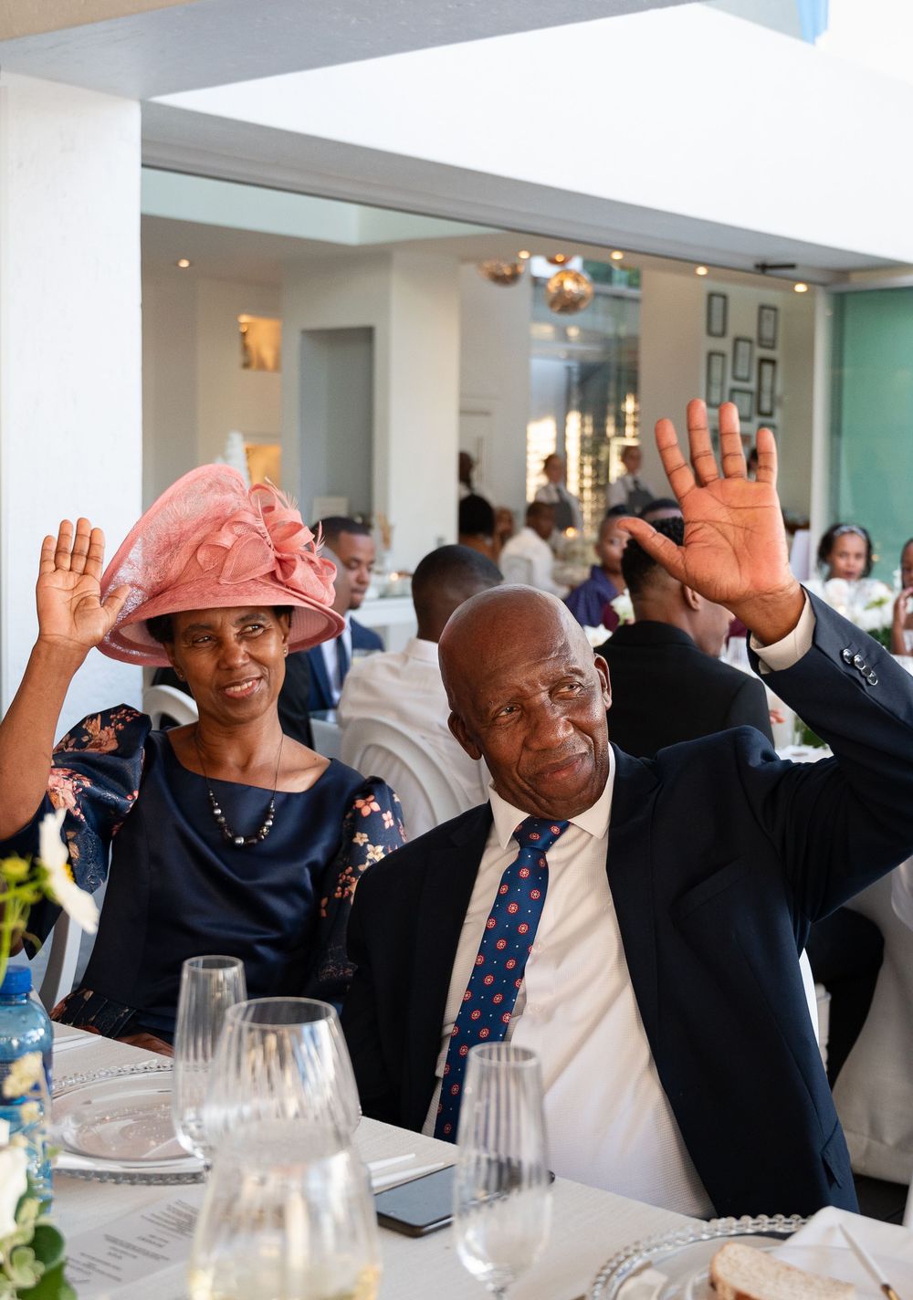 People at a formal dinner event raise their hands together in a synchronized gesture inside an elegant dining room.