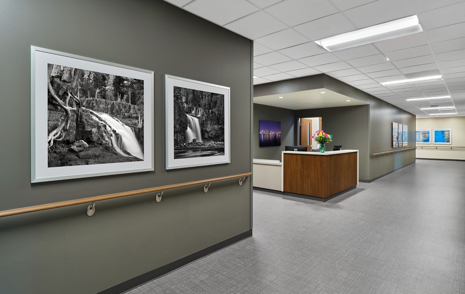 Corporate hallway featuring black and white framed photographs, wood accents, and modern lighting.