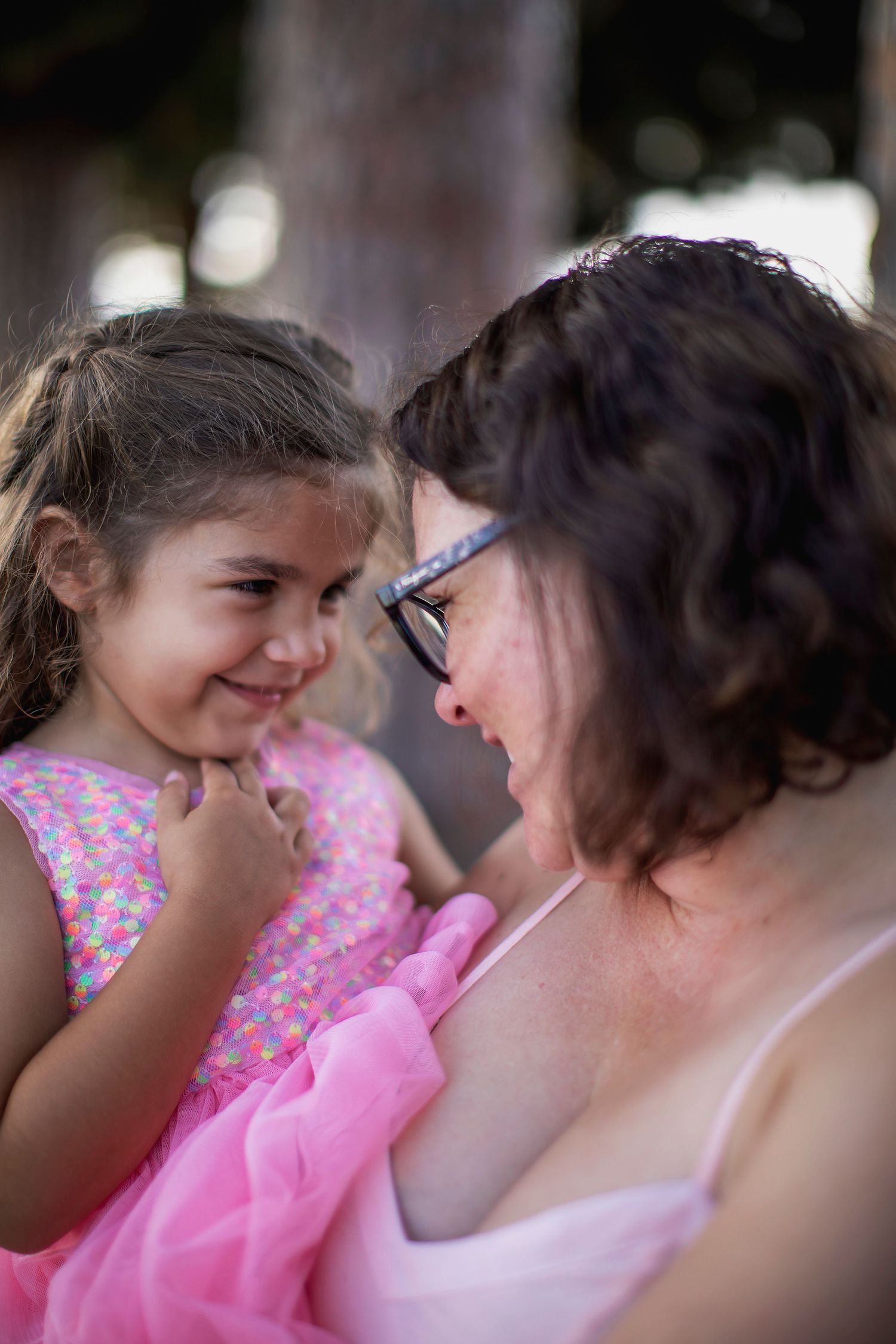 A sweet candid moment shared between adult and child wearing pink outfits while smiling at each other outdoors.