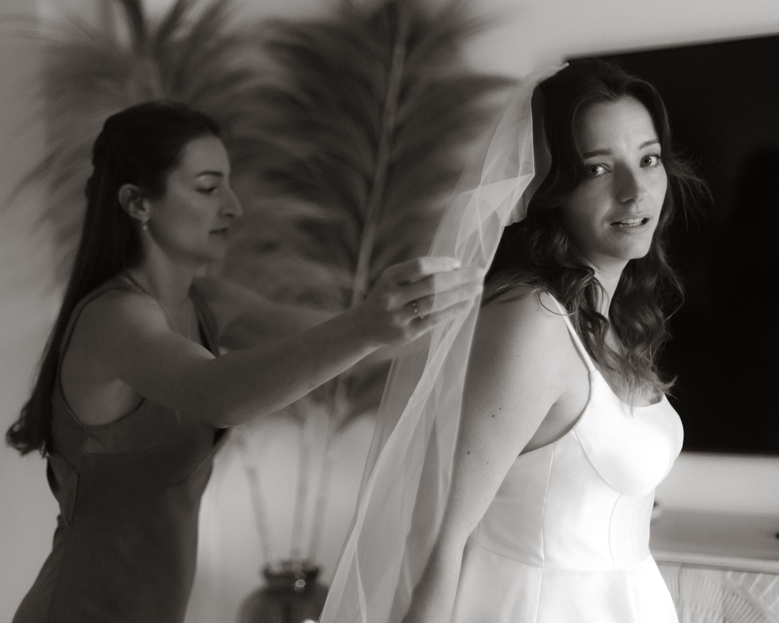 A black and white photo showing preparations for a wedding as someone adjusts a bride's veil.