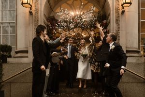 A wedding celebration outside an elegant stone archway decorated with twinkle lights and floral arrangements.