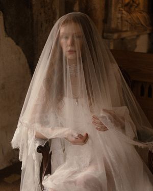 A figure in a white wedding veil poses in a dimly lit room creating a haunting, ethereal atmosphere.