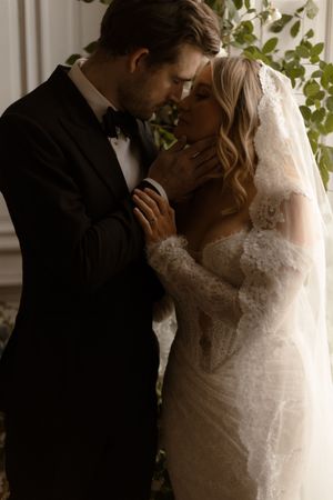 A tender moment between newlyweds as they embrace, with the bride in a lace gown and veil and groom in classic tuxedo.
