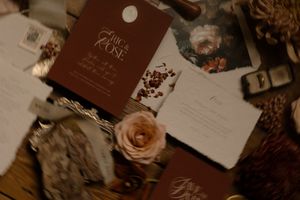 Wedding stationery in burgundy and white with dried roses and delicate floral details laid out on a wooden surface.