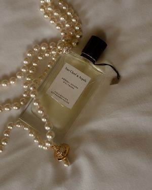 Luxurious pearl necklace draped elegantly beside Van & Stars perfume bottles on white silk fabric with soft lighting.