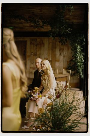 A romantic wedding couple shares an intimate moment in a rustic wooden venue with soft lighting and greenery.