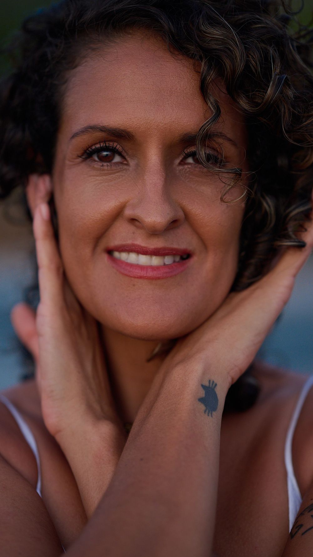 A series of four close-up portraits showing joyful expressions and curly hair with hands framing the face against a blurred background.