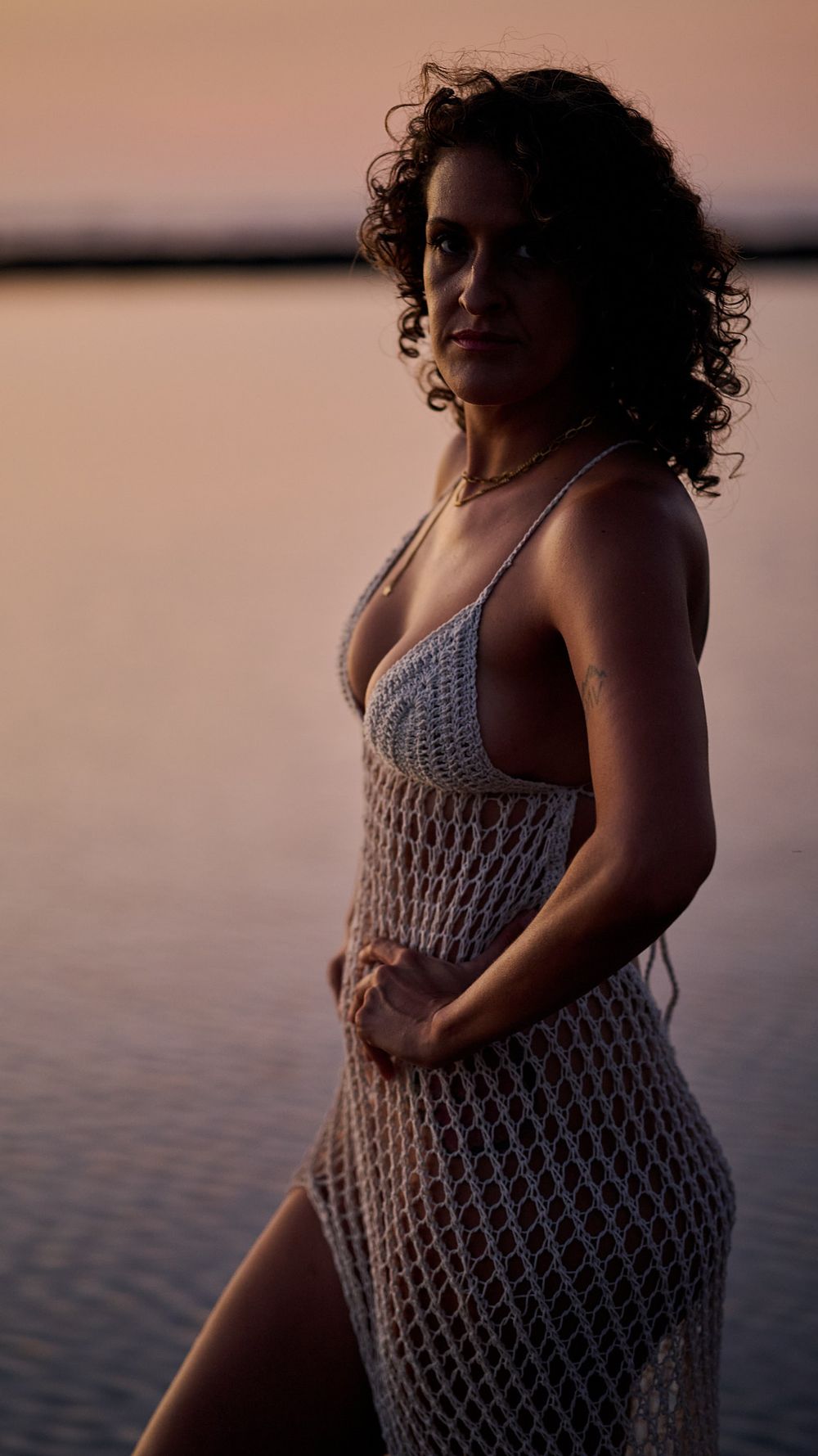 A serene maternity photoshoot at sunset shows four artistic silhouettes of a pregnant figure in a crocheted dress by the water.