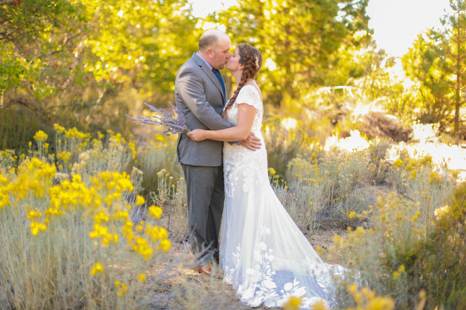A romantic wedding couple embraces in a golden field at sunset with yellow wildflowers in the background.