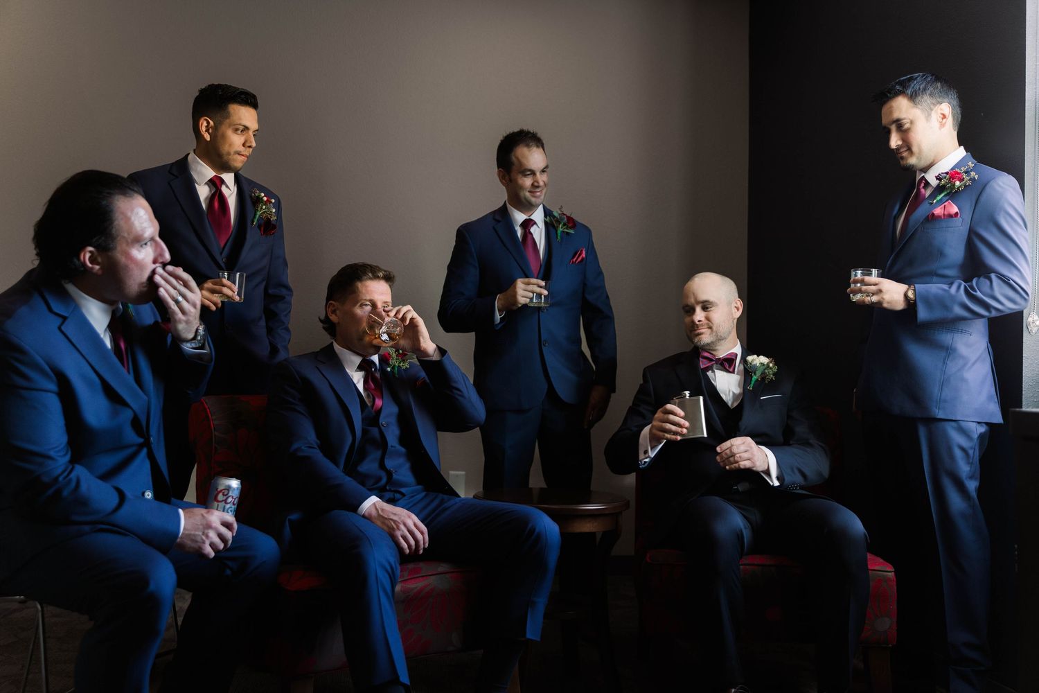 Wedding party in blue suits seated on red chairs in dramatic lighting.