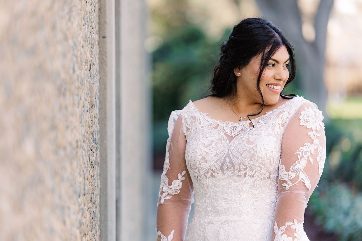 Bride in lace sleeve wedding gown smiling in outdoor portrait series.