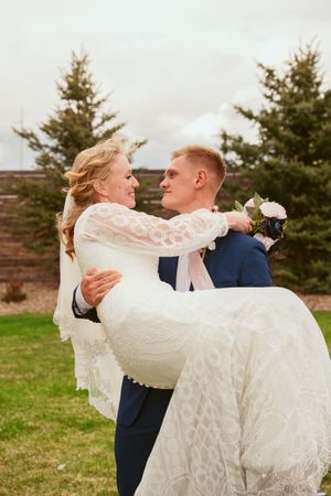 Groom in navy suit spins bride in lace dress during outdoor wedding photoshoot.