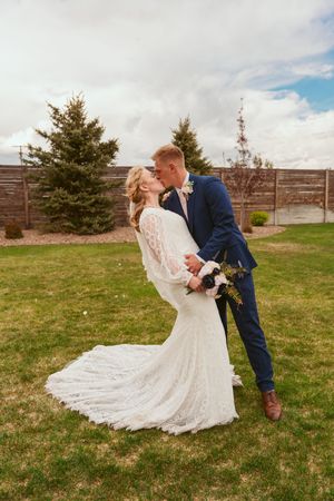 A dramatic dip kiss between newlyweds in a garden setting with the bride's lace dress trailing beautifully.