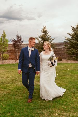 A candid moment of newlyweds walking together on grass, with the bride in lace and groom in navy suit.
