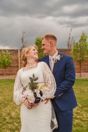 A romantic outdoor wedding portrait with cloudy skies as backdrop, featuring a couple in navy and white attire.