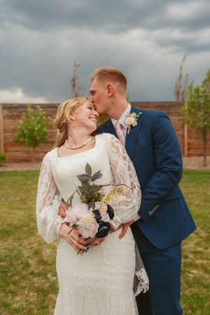 Couple shares romantic moments in garden setting with cloudy sky backdrop.