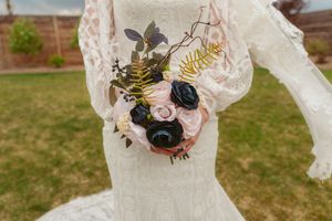 Close up of a bridal bouquet with pink and black roses against white lace dress.