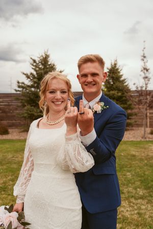 A romantic wedding moment captured outdoors with trees and a rustic wooden wall in the background.