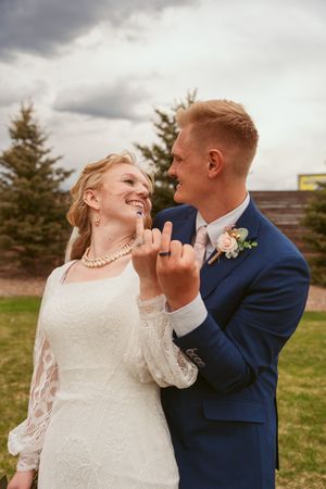 A playful wedding moment captured outdoors with the couple laughing and showing off their rings.