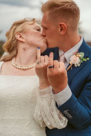 A romantic wedding photo moment showing raised hands displaying wedding rings while sharing a kiss.
