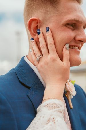 Close up of engagement ring displayed on hand against navy blue suit jacket.