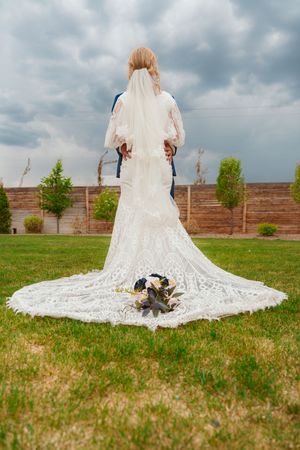 A long white lace wedding dress with a dramatic cathedral train spreads across a green grassy field.