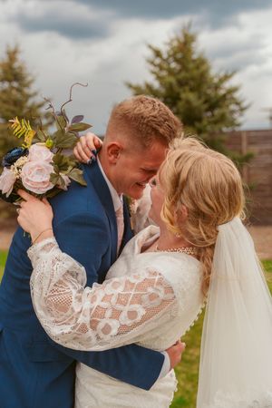 A romantic wedding moment captured outdoors with the bride in lace sleeves and groom in navy suit sharing a tender embrace.