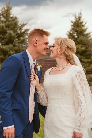 A romantic wedding moment between newlyweds in front of evergreen trees.