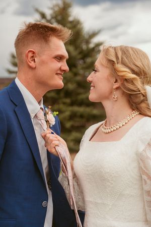 A romantic wedding portrait of a couple in formal attire, with the bride wearing pearls and a white dress outdoors.