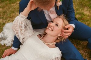 A joyful moment captured between newlyweds laying in grass wearing traditional wedding attire.