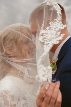 Wedding couple sharing an intimate kiss under a delicate lace veil at their outdoor ceremony.