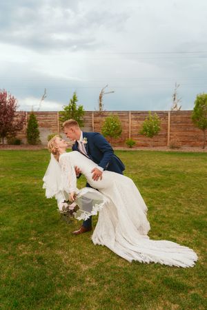 A wedding couple dips dramatically on a grassy lawn with cloudy skies in the background.