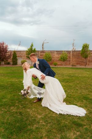 Dramatic dip poses of couple on grassy lawn showing flowing white wedding dress train.