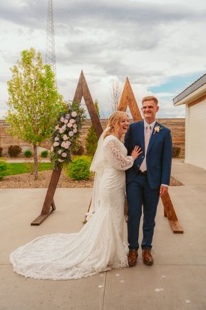 Wedding couple poses in front of a wooden triangle arch decorated with pink flowers.