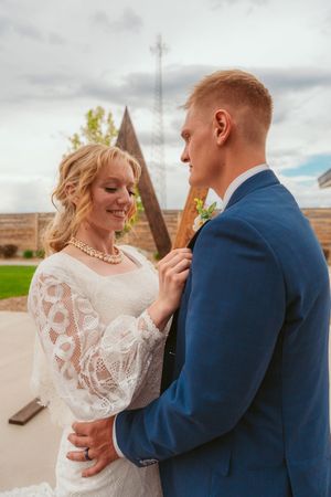 A romantic wedding dance scene outdoors with the bride in lace and groom in navy blue suit against a cloudy sky.