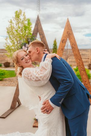 Romantic couple shares intimate moment in front of wooden triangle backdrop at outdoor venue.