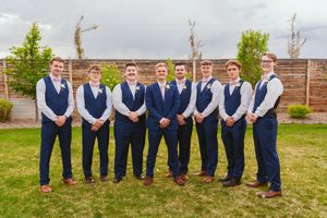Wedding party in navy blue and pink attire poses together on a grassy lawn with brick wall backdrop.