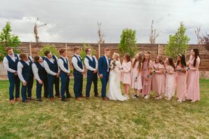 Bridal party stands in a row wearing navy and pink attire against rustic outdoor setting.