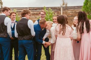 Wedding party in navy blue suits and pink dresses laughing together outdoors.