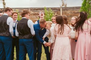 Wedding party shares a laugh together in outdoor garden setting with bridesmaids in pink dresses.