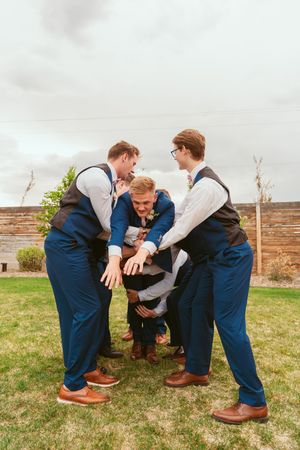 Groomsmen in navy suits and vests playfully posing together outdoors.