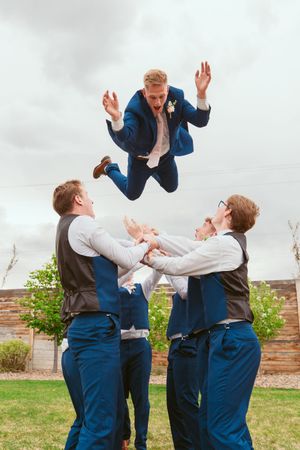 A groomsman and best man perform dramatic poses in navy suits and brown vests during a fun wedding photoshoot.